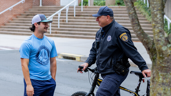 A public safety officer with his bike speaks with a student outside